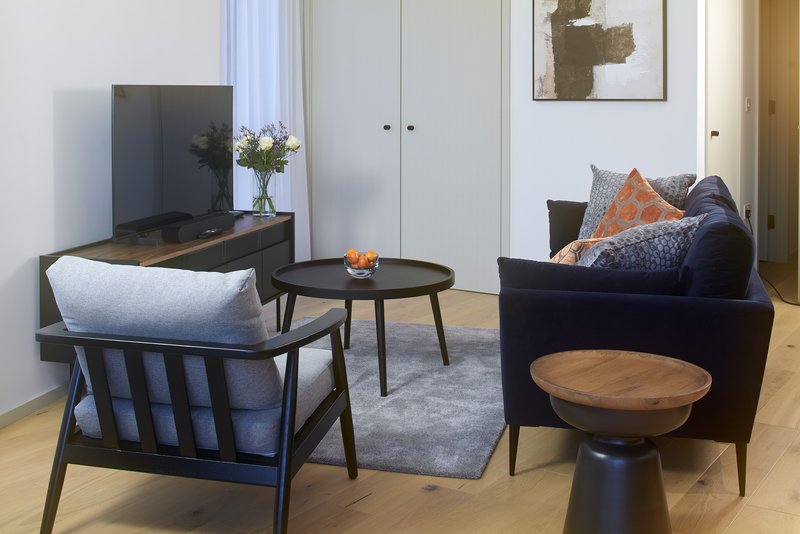 Modern living room with black armchairs, TV, wooden side table, and abstract wall art