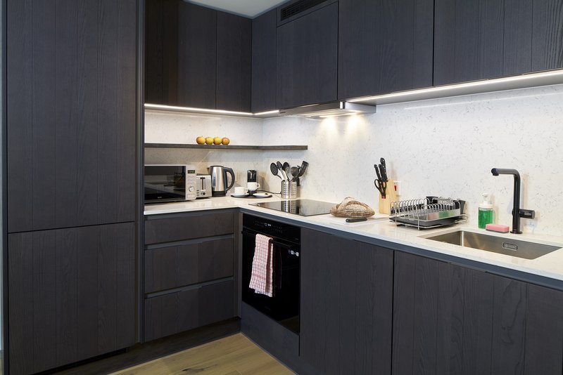Modern kitchen with dark cabinetry, white countertop, integrated appliances and pendant lighting