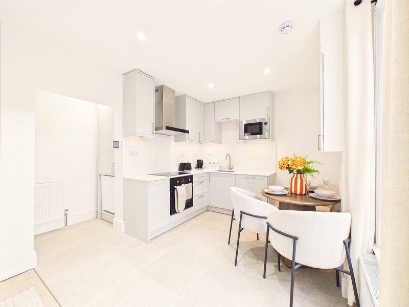 Modern white kitchen with dining table, stove, and bright natural lighting from window