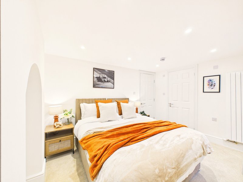 Bright bedroom with double bed, orange throw, wooden bedside table and framed wall art