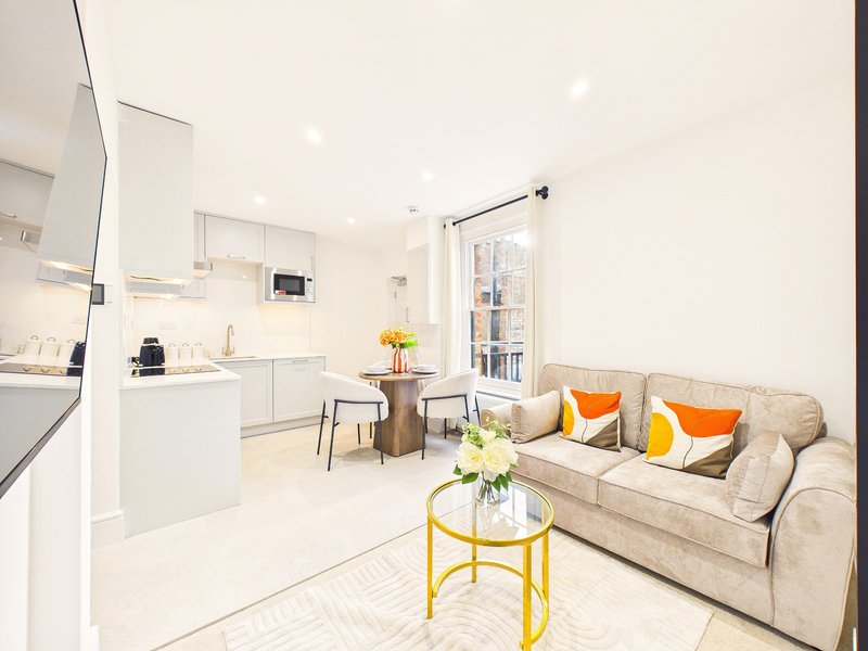 Open-plan kitchen and living room with white cabinetry, beige sofa, dining table and glass doors