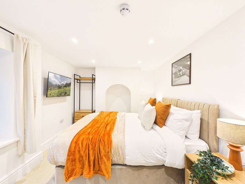 Modern bedroom with double bed, orange throw, white bedding and neutral headboard
