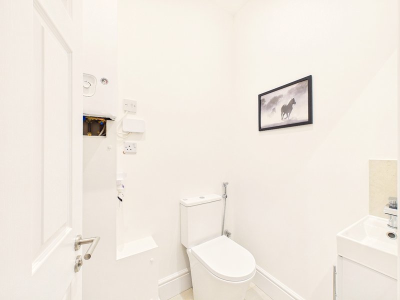 Small white bathroom with toilet, sink, mirror and framed wall art
