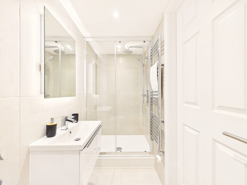 Modern white bathroom with double sink, large mirror, walk-in shower and heated towel rail