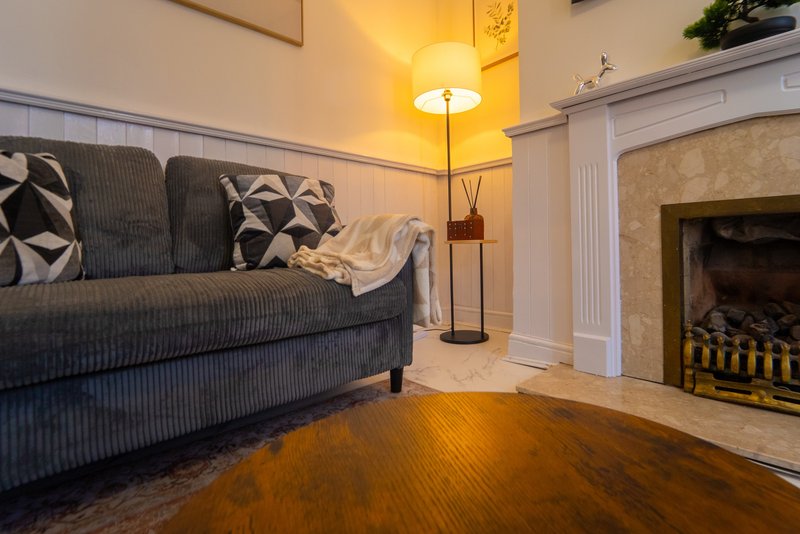 Living room with grey upholstered sofa, fireplace with brass fender, wooden floor and floor lamp