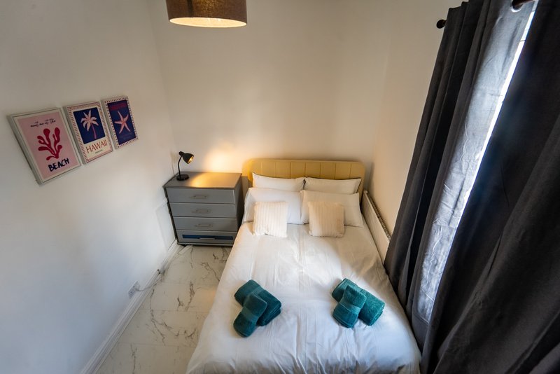 Compact bedroom with single bed, teal cushions, bedside table, wall art and dark curtains