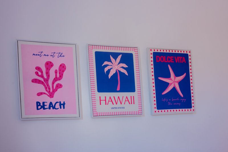 Three framed colorful wall prints with beach and Hawaii themed designs on light purple wall