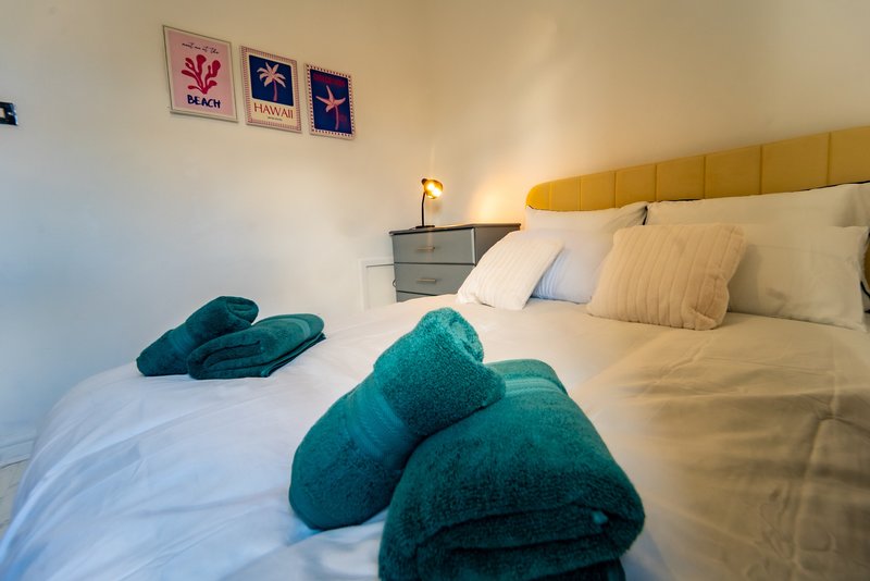Bedroom with yellow headboard, white bedding, teal towels, and framed wall art