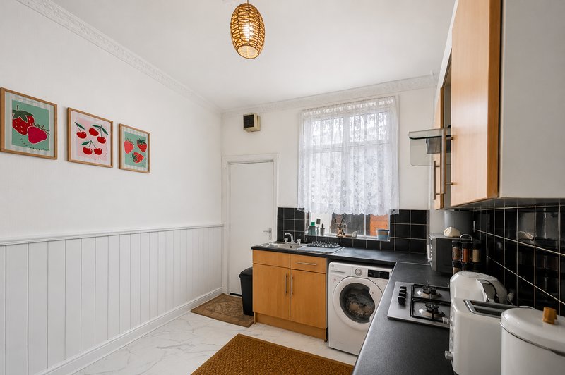 Kitchen with white walls, wooden cabinets, washing machine, black tile splashback and window