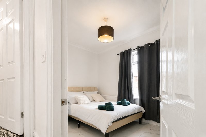Bright bedroom with double bed, wooden headboard, black curtains and ceiling light fixture