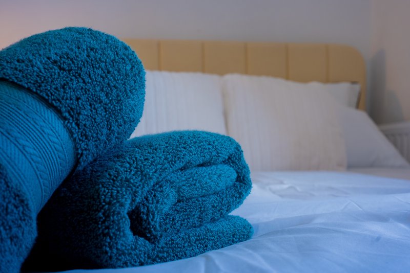 Rolled teal towels on bed with white pillows and upholstered headboard