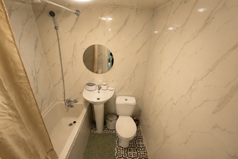Compact bathroom with marble-effect tiles, pedestal sink, toilet, and round mirror