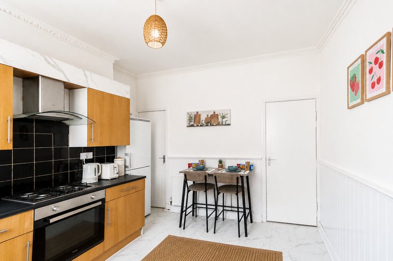 Modern kitchen with wooden cabinets, black backtile, and adjoining dining area with bar stools