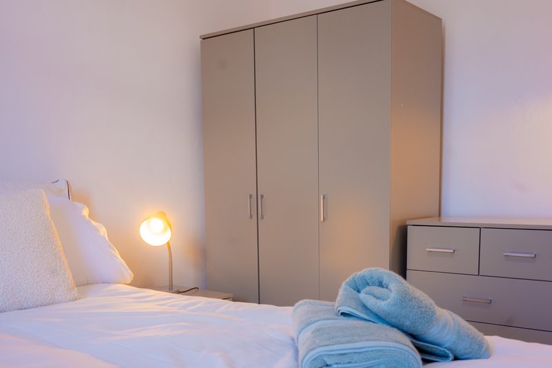 Modern bedroom with double bed, wardrobe, bedside lamp and folded blue towels