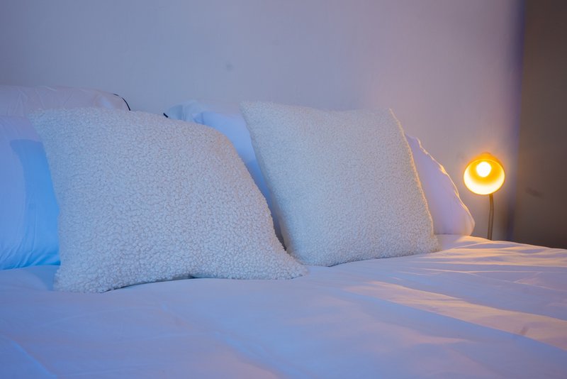 Bed with white pillows and bedding, warm bedside lamp lighting