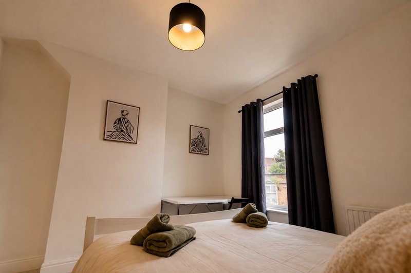 Bright bedroom with wooden floor, double bed, black curtains and ceiling light