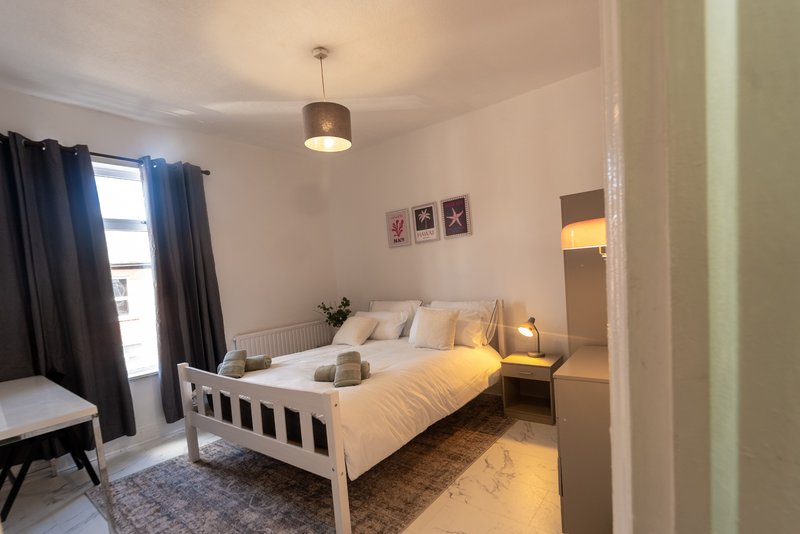 Bright bedroom with white bed frame, yellow bedding, dark curtains, pendant light, and wall art