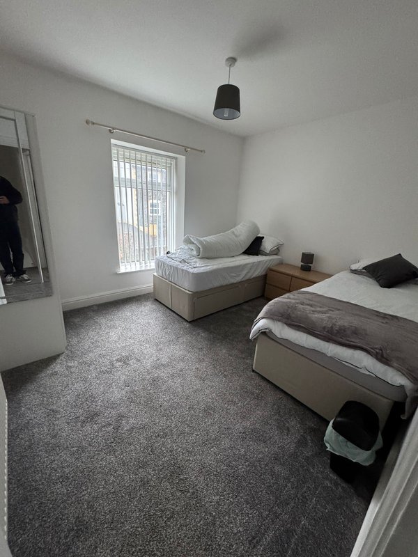 Bright bedroom with two single beds, grey carpet, pendant light and vertical blinds