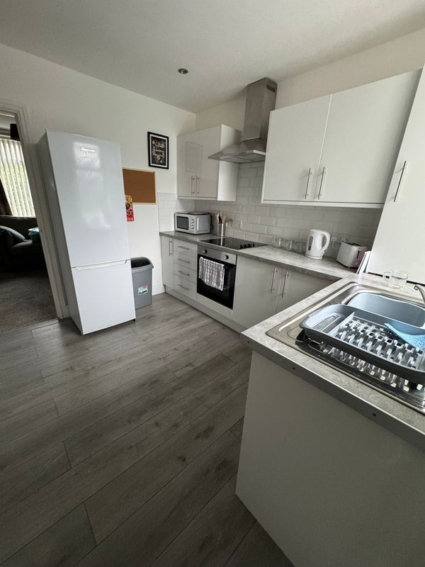 Modern kitchen with white cabinets, stainless steel appliances, grey tile backsplash and wooden floor
