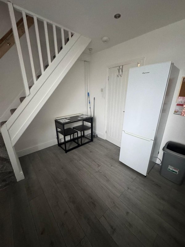 Kitchen area with white refrigerator, black shelving unit, stairs, and wooden flooring