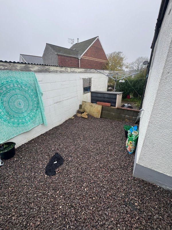 Outdoor patio area with gravel ground, white fence, turquoise decorative hanging, and brick buildings beyond