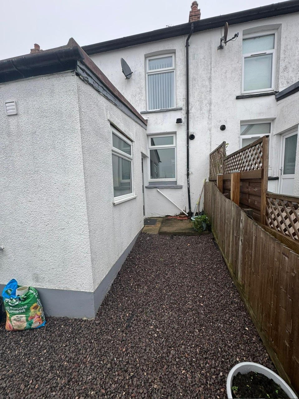 Side alley of white terraced house with gravel path, wooden fence and entry door