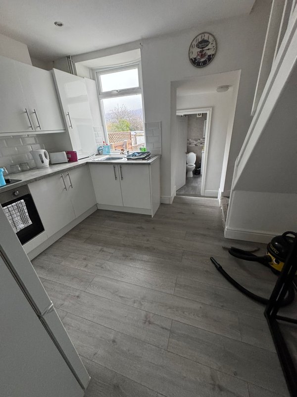 Modern kitchen with white cabinetry, grey wood-effect flooring, window and doorway to hallway