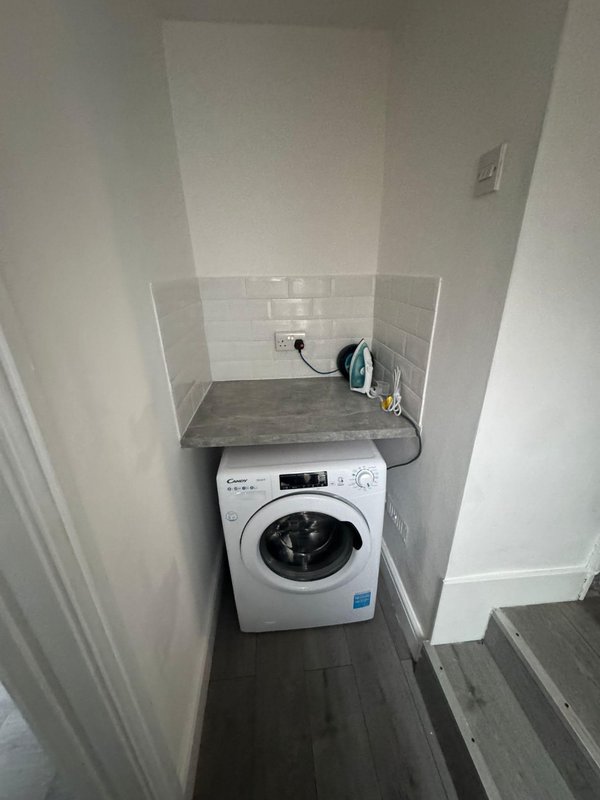 Laundry room with white front-load washing machine under grey countertop