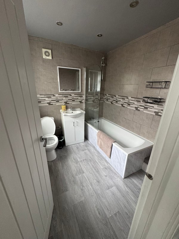 Modern bathroom with toilet, vanity sink, bathtub, tiled walls and recessed lighting