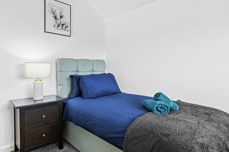 Bedroom with blue bedding, grey headboard, dark wooden nightstand and lamp