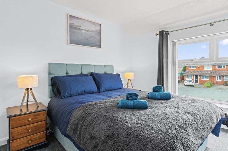 Bright bedroom with double bed, green headboard, blue bedding, and views of suburban street