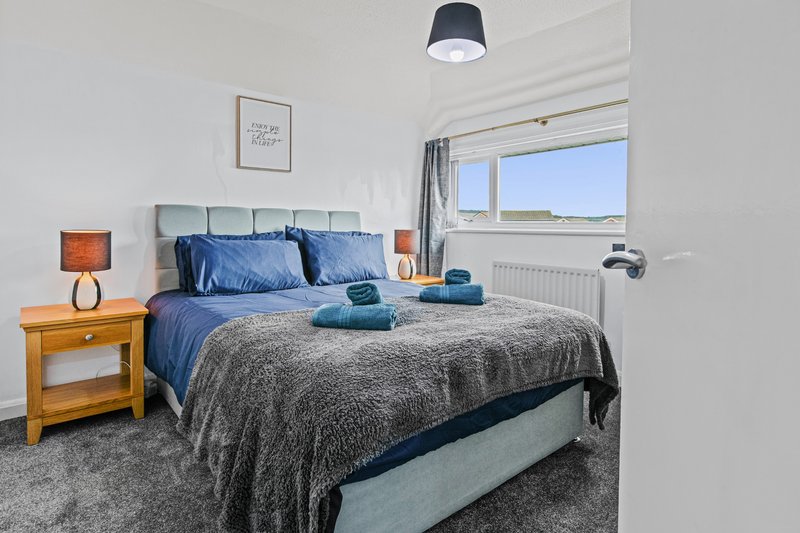 Bright bedroom with double bed, blue bedding, wooden nightstand, and large window