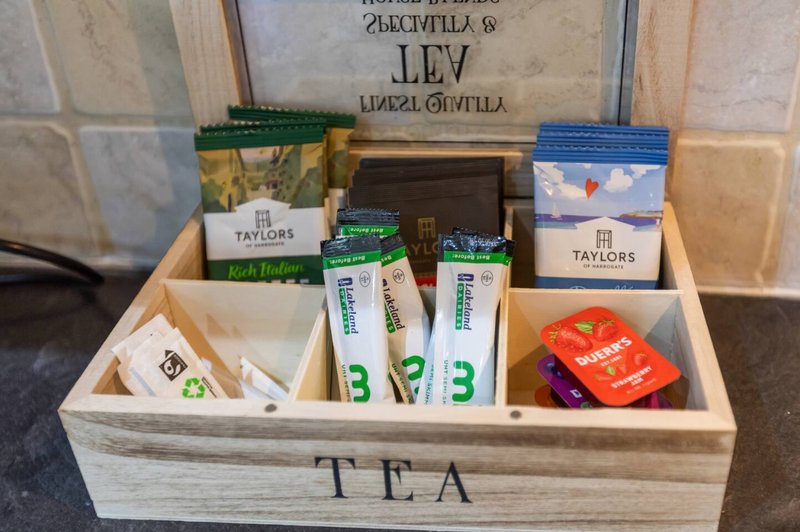 Wooden tea caddy with assorted tea bags, coffee sachets, and branded packaging organized in compartments