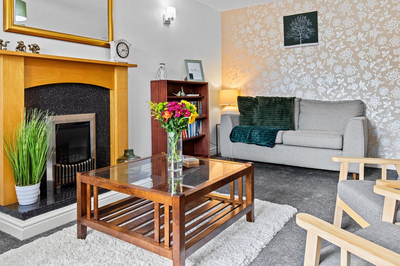 Bright living room with fireplace, wooden coffee table, grey sofa and floral wallpaper