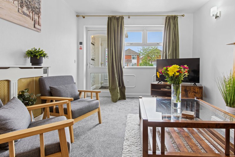 Bright living room with wooden furniture, grey upholstered chairs, glass coffee table and garden views