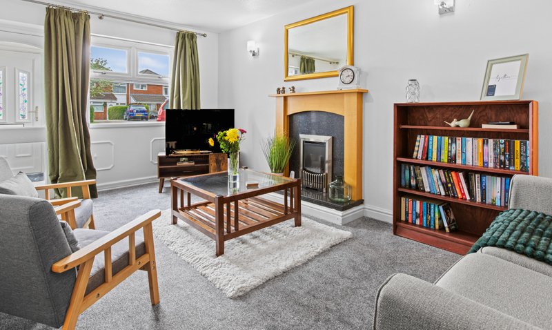 Bright living room with wooden furniture, fireplace, bookshelf, TV, and garden views