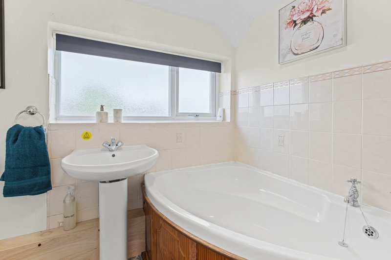 Bright bathroom with pedestal sink, oval bathtub, wooden cabinetry, and large window