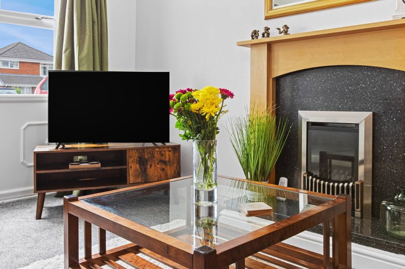 Living room with wooden coffee table, TV on stand, fireplace and fresh flowers in vase