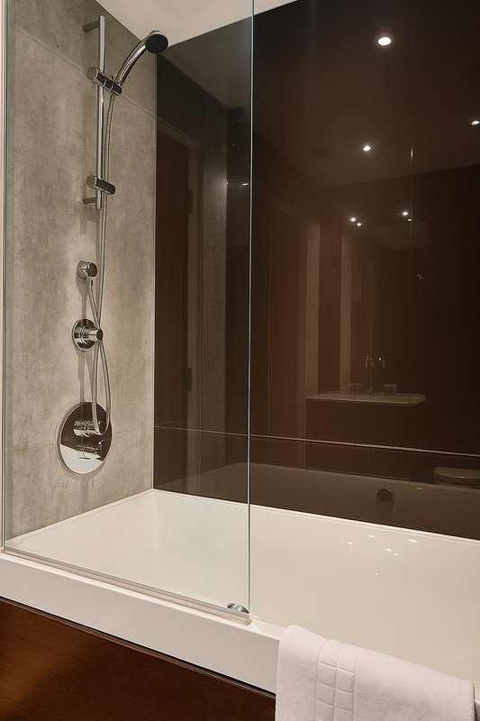 Modern bathroom with walk-in shower, glass screen, white tub and dark tile walls