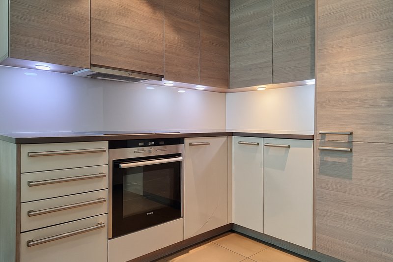 Modern kitchen with white and wood cabinetry, built-in oven, and LED under-cabinet lighting