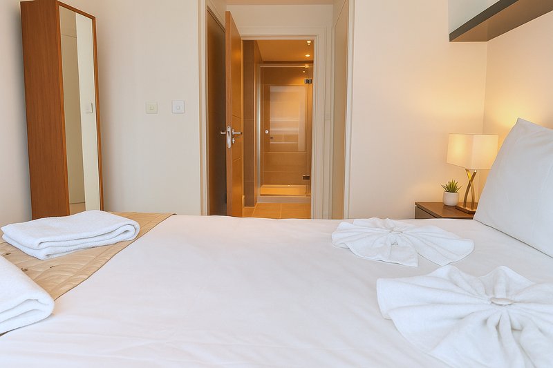 Modern bedroom with double bed, white bedding, wooden doors, mirror, and bedside lamp