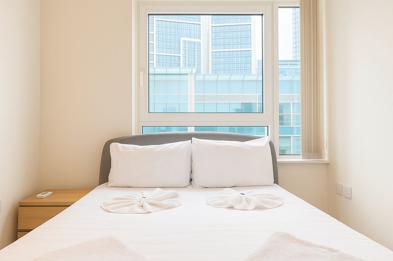 Modern bedroom with double bed, grey headboard, white bedding, wooden nightstand and city views