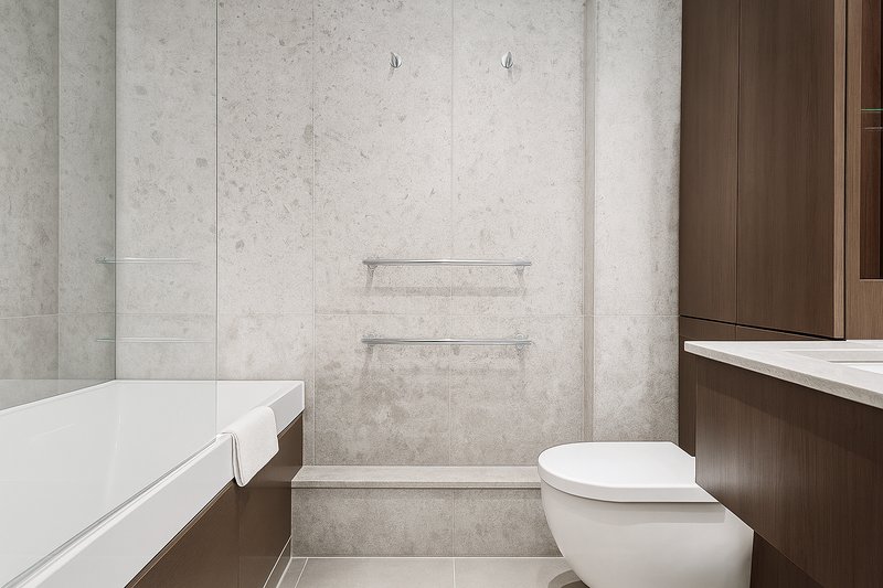 Modern bathroom with white toilet, bathtub, concrete-effect wall tiles and wooden vanity