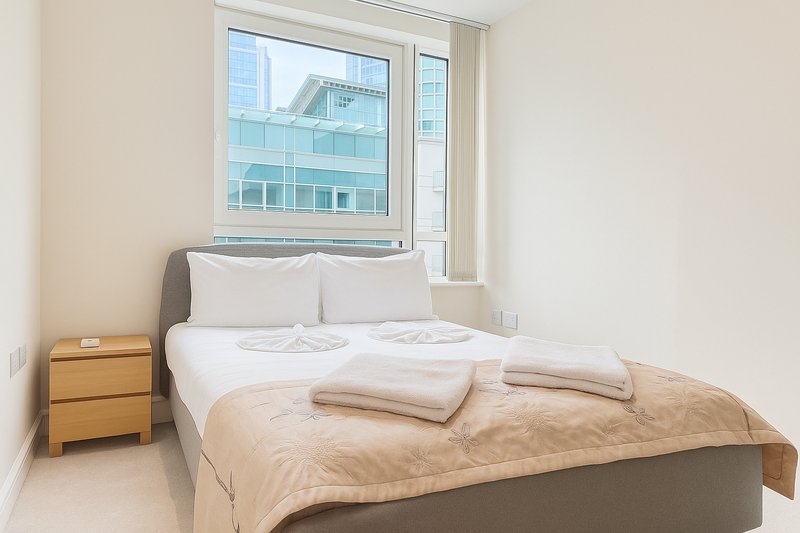 Bedroom with double bed, wooden nightstand, large window overlooking city buildings