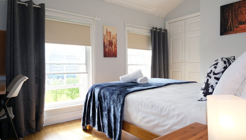 Bright bedroom with double bed, blue bedding, windows with dark curtains and countryside view