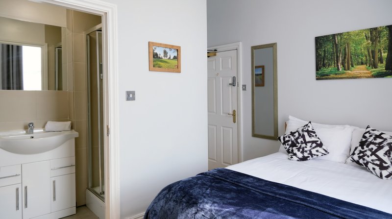 Bedroom with double bed, navy bedding, black and white cushions, ensuite bathroom visible