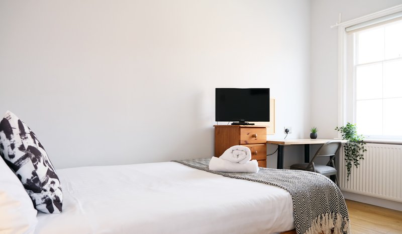 Bright bedroom with double bed, wooden TV stand, small plant, and window with natural light