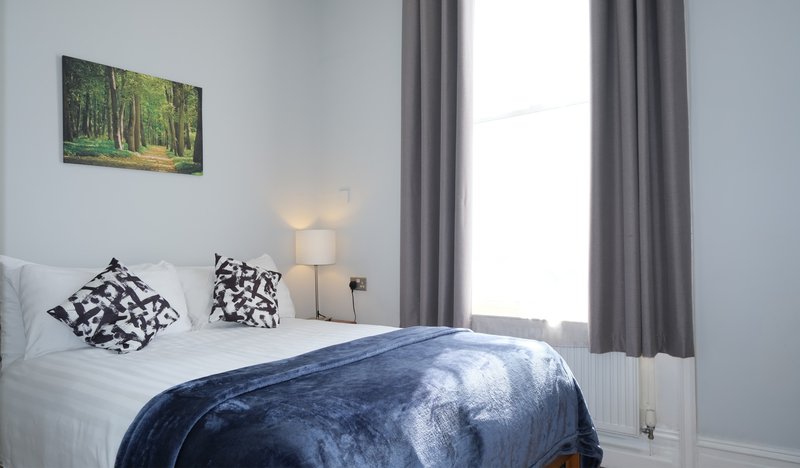 Bright bedroom with double bed, patterned cushions, bedside lamp and forest artwork