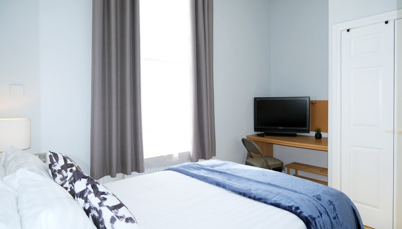 Bright bedroom with double bed, wooden desk, TV, grey curtains and white door