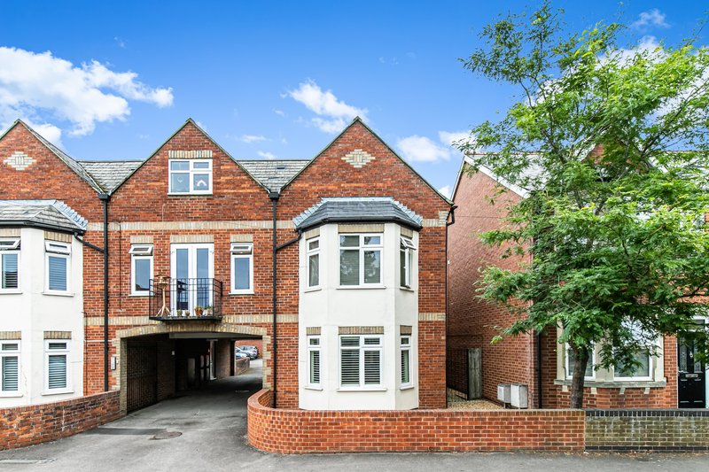 Red brick residential building with white trim, driveway, and mature green foliage